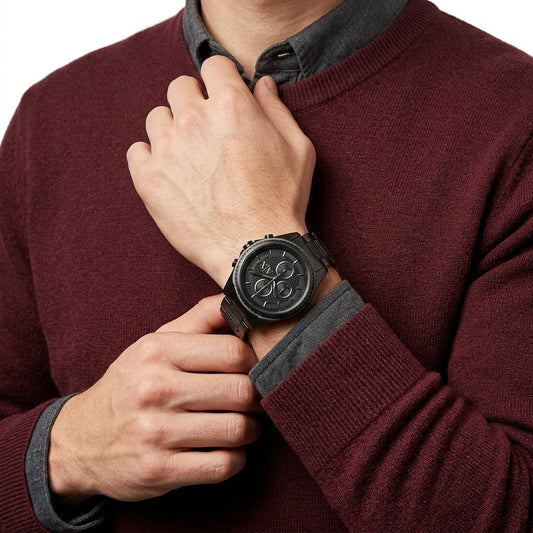 A close-up of a man wearing a black multi-dial wristwatch with a dark strap, dressed in a maroon knit sweater over a dark gray collared shirt.