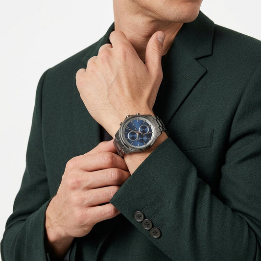 A close-up of a man wearing a dark green blazer, showcasing a silver-toned chronograph watch with a blue dial and matching blue bezel on his wrist.