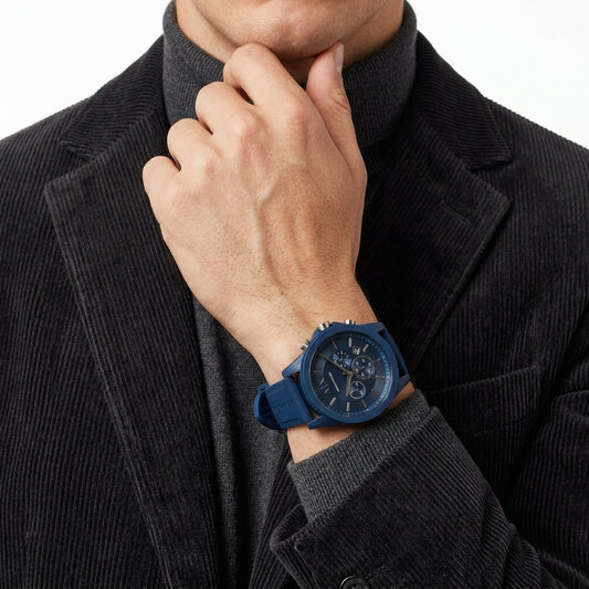 A men's sport watch with a dark blue silicone strap and a matching dark blue dial, shown on a model's wrist wearing a dark corduroy jacket and grey turtleneck.