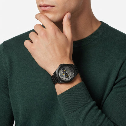 A close-up of a man wearing a dark green knit sweater and a black wristwatch with a black metal strap and a detailed dark dial.