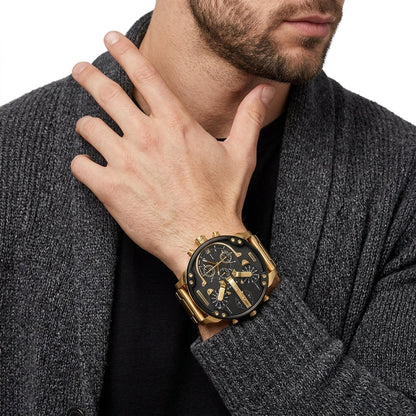 A close-up of a man wearing a gold-tone chronograph watch with a black dial and gold bracelet, styled with a dark gray knit cardigan over a black shirt.